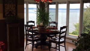 A dining area with a table set for four, surrounded by large windows offering a view of a body of water. - Pictured Rocks Bed And Breakfast (Munising)