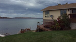 A house with a deck overlooking a lake, a satellite dish, and a view of distant hills. - Pictured Rocks Bed And Breakfast (Munising)