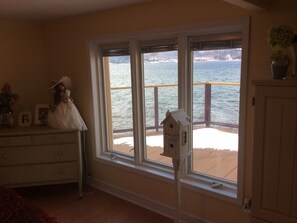 A room with a large window overlooking a body of water, a dresser with personal items, and a small birdhouse on the windowsill.