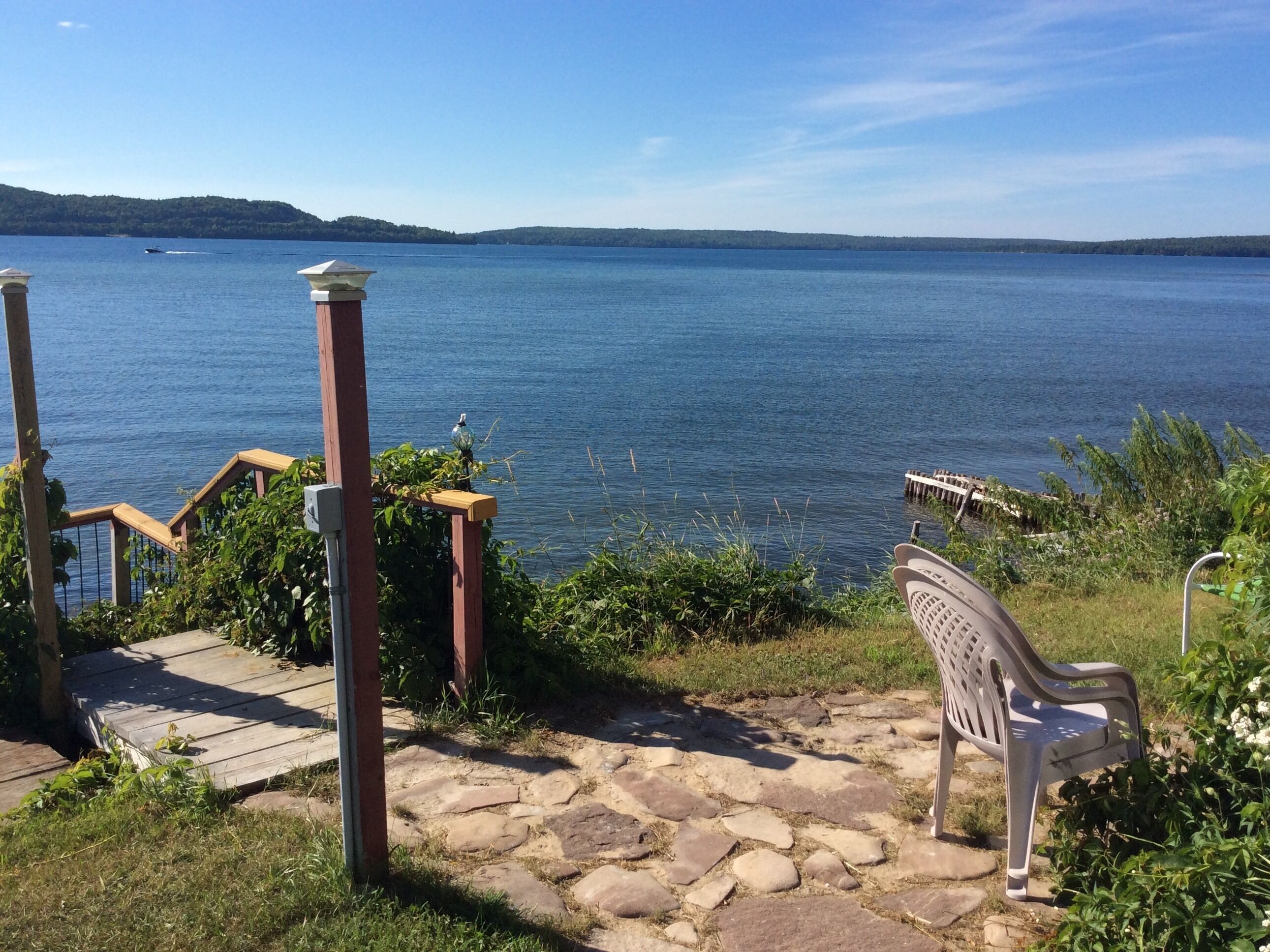 A stone pathway leading to a bench overlooking a lake with a wooden dock and a boat in the distance.