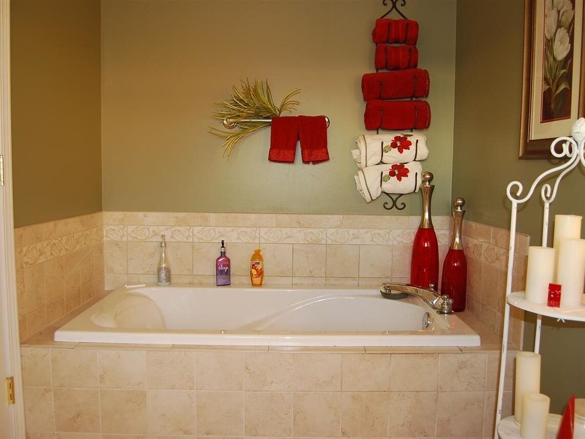 A bathroom with a bathtub, a towel rack with red towels, a shelf with candles, and toiletries.