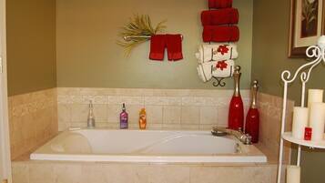A bathroom with a bathtub, a towel rack with red towels, a shelf with candles, and toiletries.
