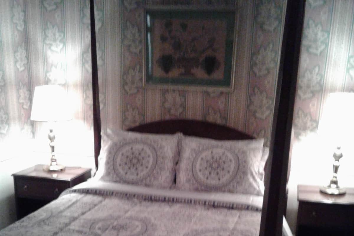 A four-poster bed with a patterned bedspread, two bedside tables with lamps, and a framed picture on the wall.