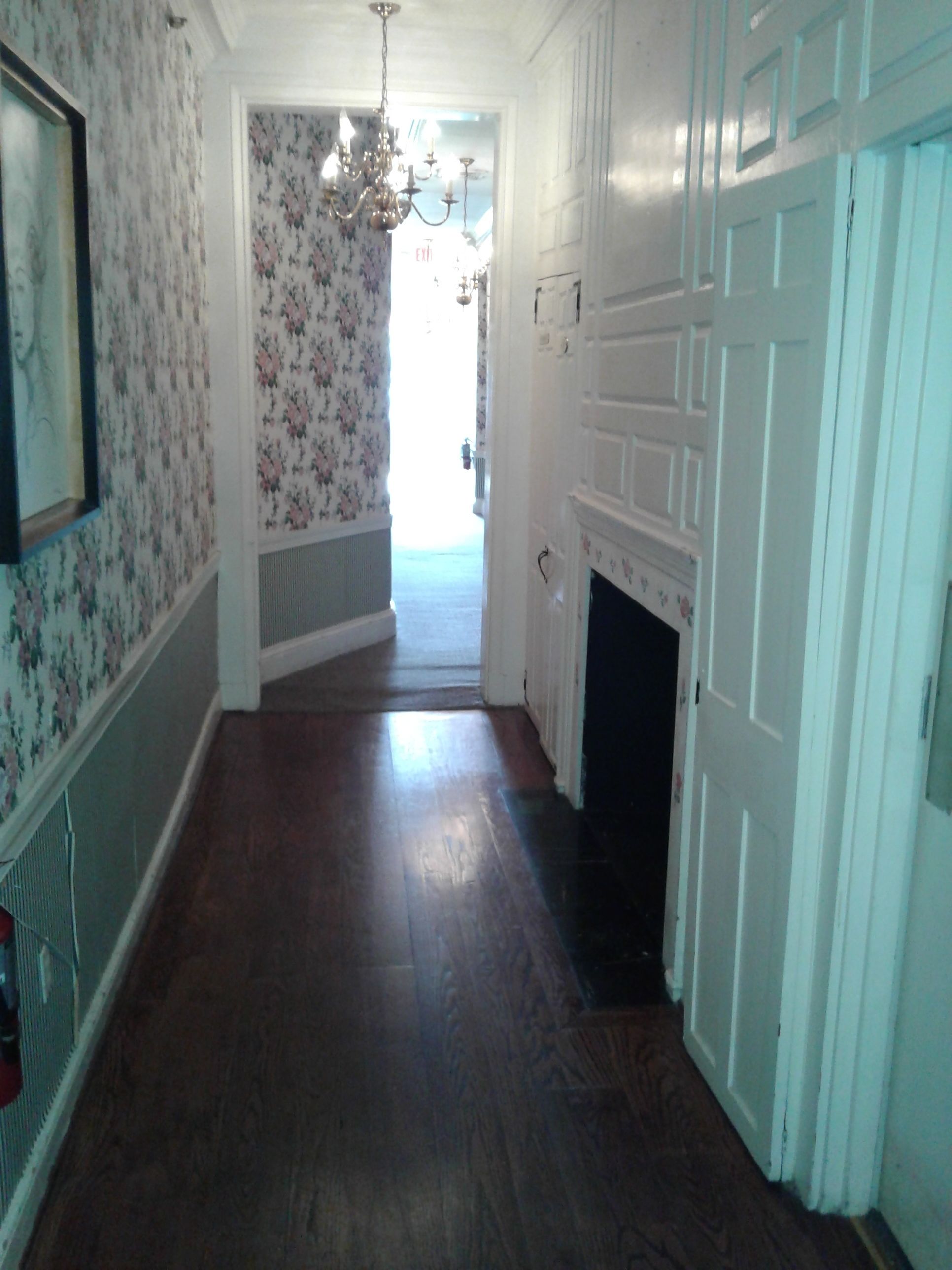 A hallway with floral wallpaper, a chandelier, and a fireplace.