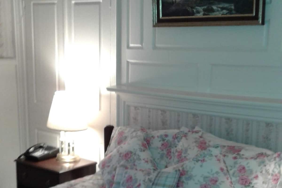 A bedroom with a bed, a nightstand, a lamp, and a painting on the wall.
