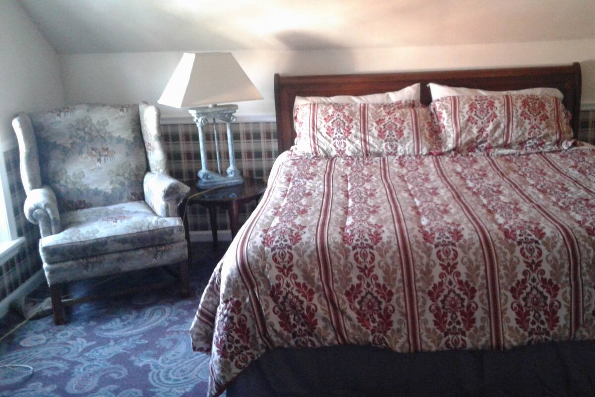 A bedroom with a large bed, a chair, two lamps, and a patterned carpet.