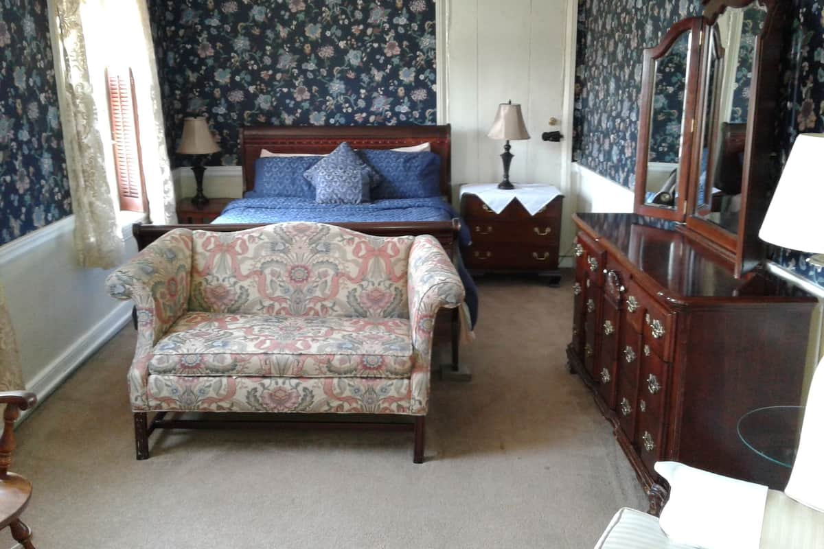 A bedroom with a bed, a chair, a dresser, and a mirror.