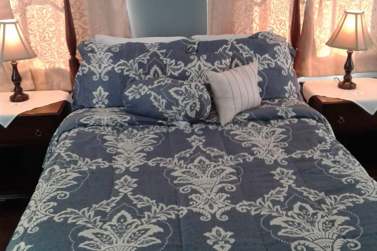 A bed with a patterned blue and white duvet, two bedside lamps, and curtains with a floral pattern.