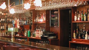 A bar area with a wooden counter, shelves with bottles, and hanging wine glasses. - The Brick Hotel (Newtown)