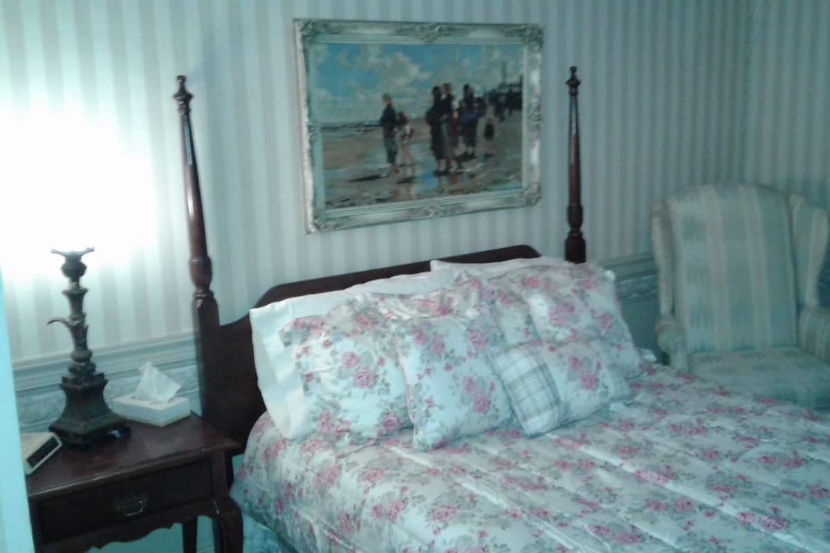 A bedroom with a bed, a nightstand, a chair, and a painting on the wall.