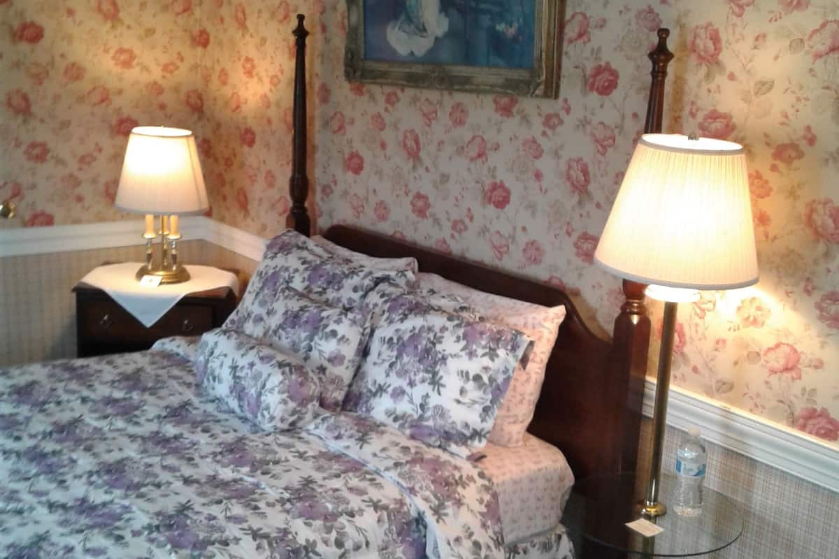 A bedroom with floral wallpaper, a bed with floral bedding, two bedside lamps, and a framed picture on the wall.