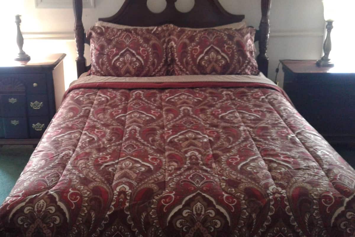 A four-poster bed with a red and gold patterned bedspread and matching pillows.