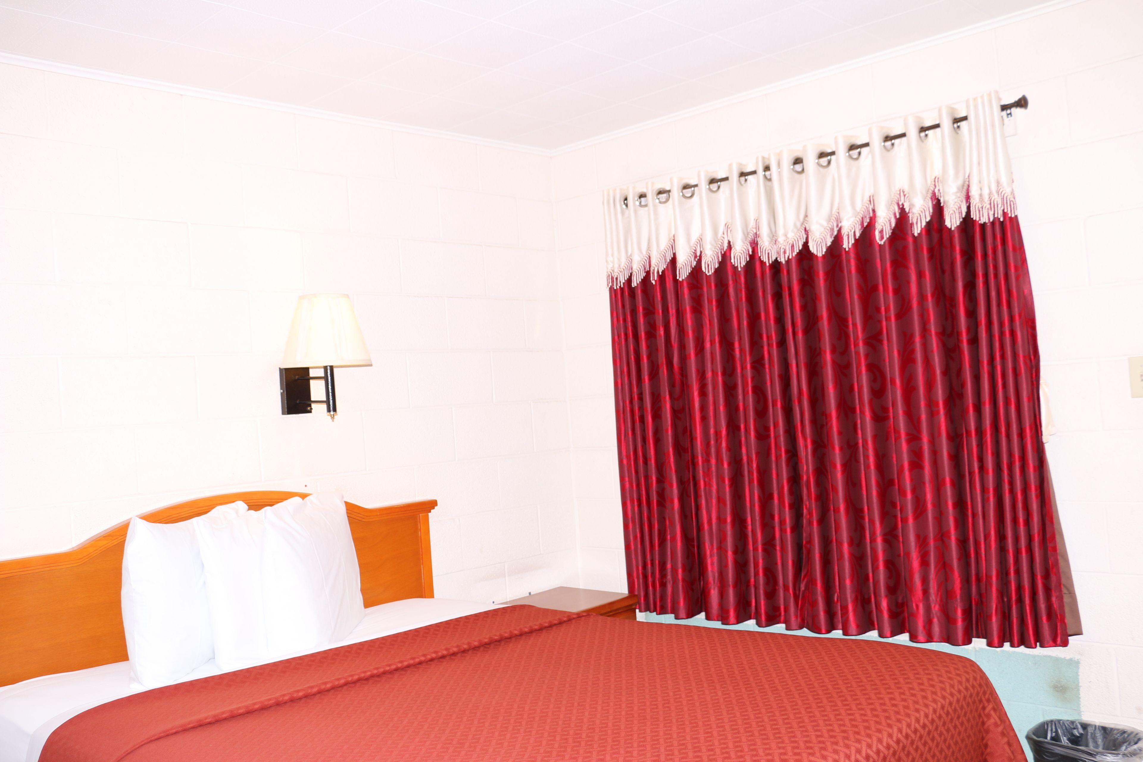 Ein Hotelzimmer mit einem Bett, weißen Wänden, einem roten Vorhang und einer Lampe.
