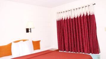 Ein Hotelzimmer mit einem Bett, weißen Wänden, einem roten Vorhang und einer Lampe.