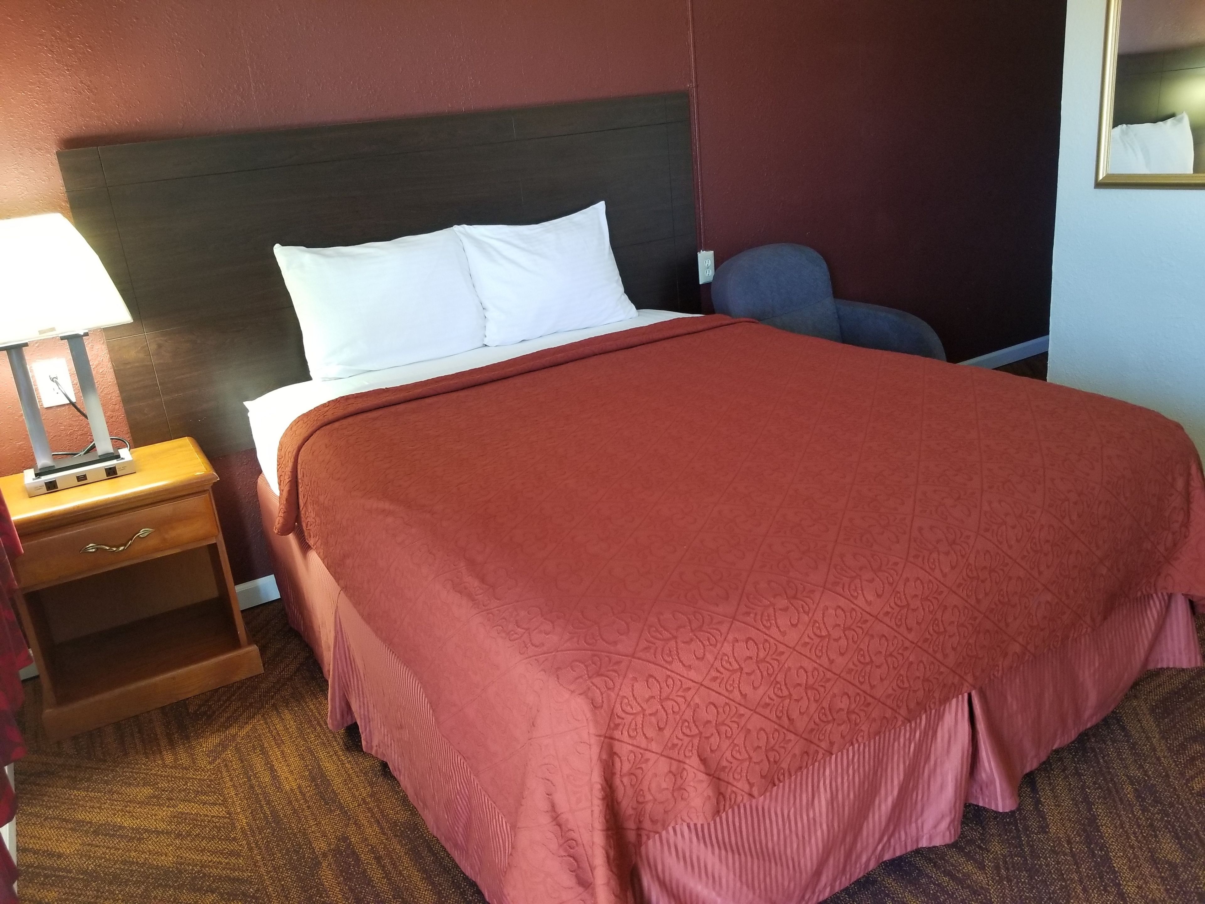 A hotel room with a large bed, a nightstand with a lamp, and a chair.