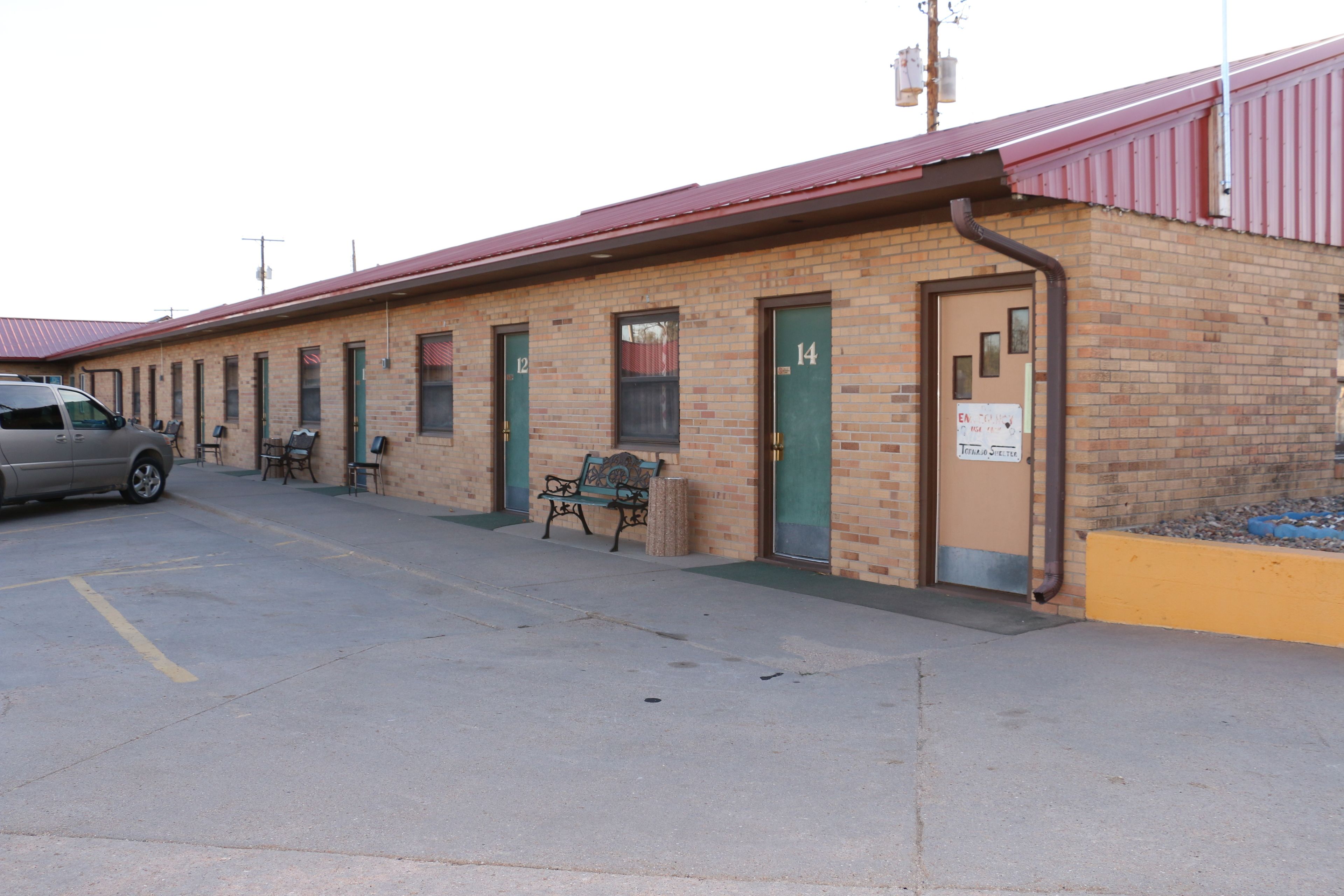 A single-story motel with numbered rooms, a parking area, and a bench outside.