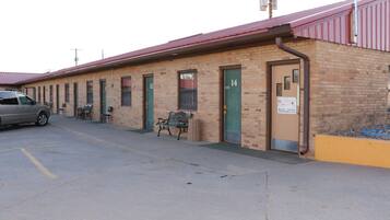 A single-story motel with numbered rooms, a parking area, and a bench outside.