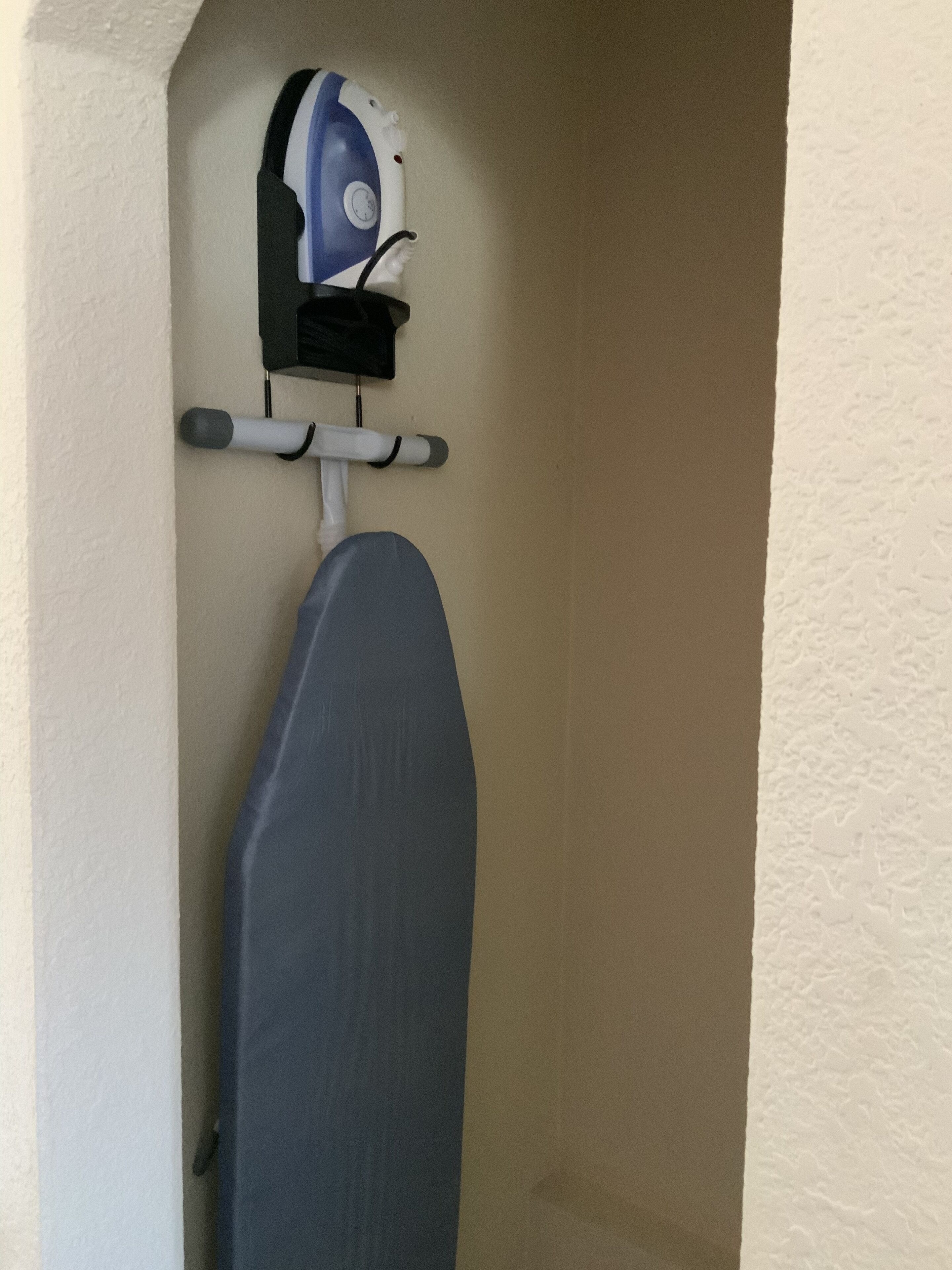 An ironing board with an iron mounted on a wall in a corner.