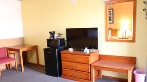 Habitación de hotel con escritorio de madera, televisor, refrigerador, banca y basurero.