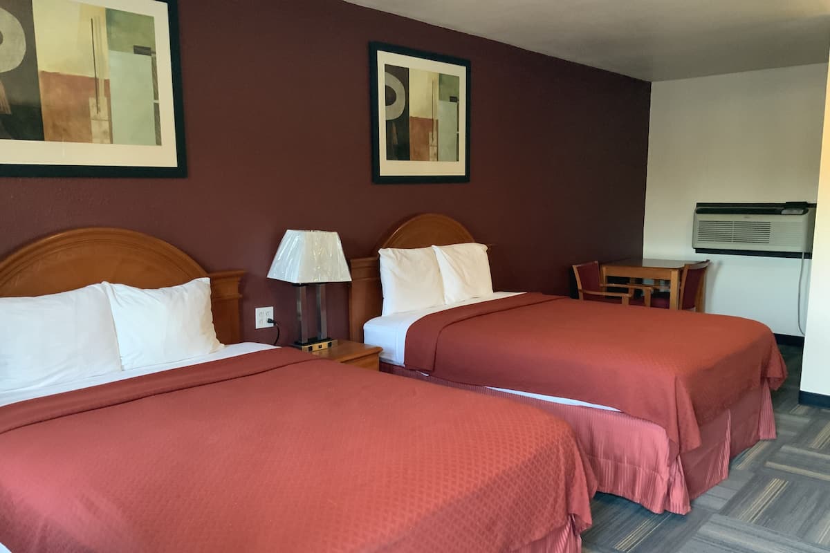 Une chambre d’hôtel avec deux lits, une table de chevet avec une lampe, une petite table et un climatiseur fixé au mur.
