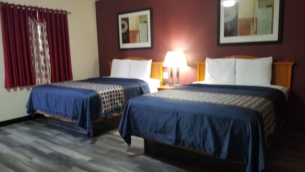 Habitación de hotel con dos camas, piso de madera, cortinas rojas y una lámpara.