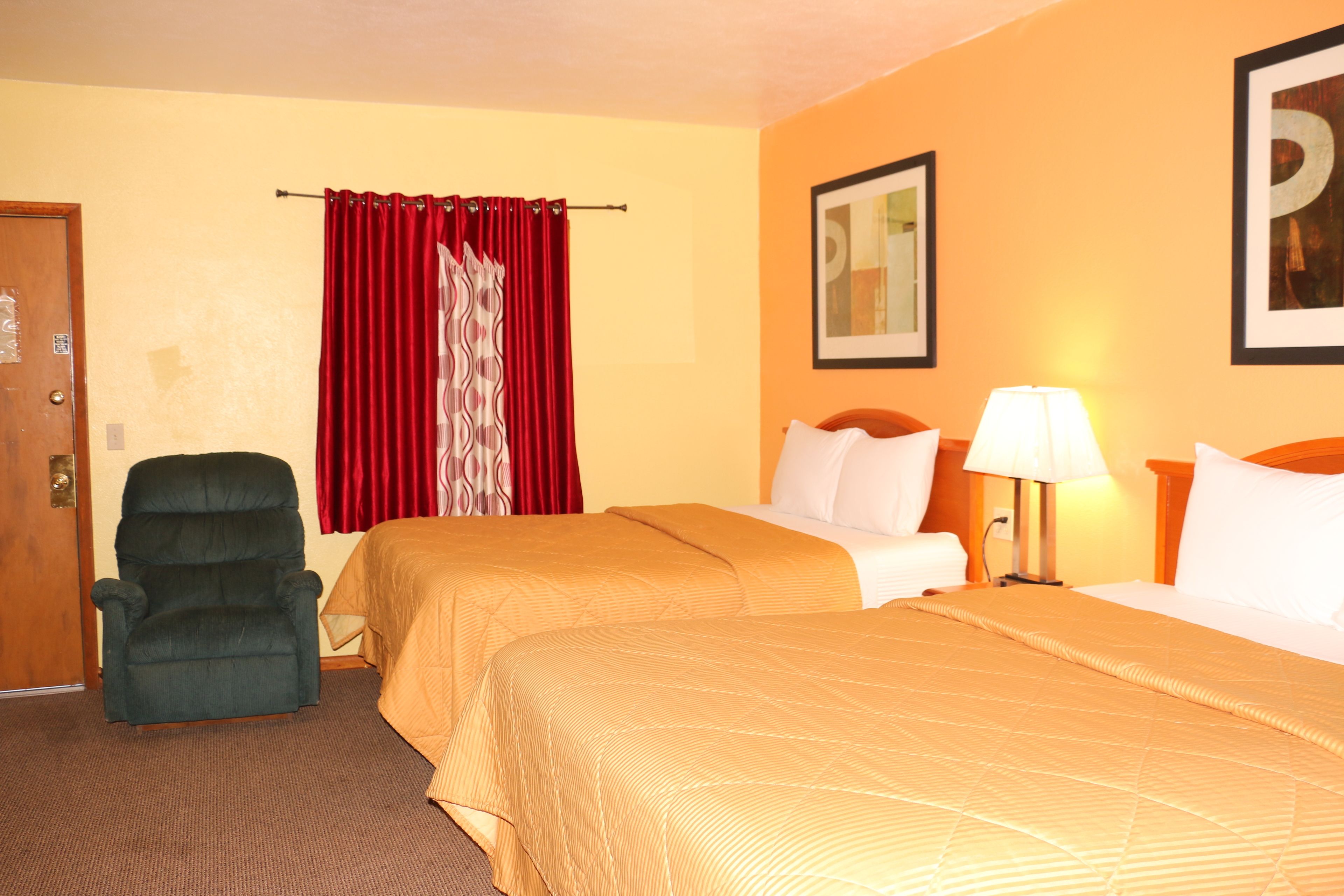 A hotel room with two beds, a chair, a lamp, and a door.