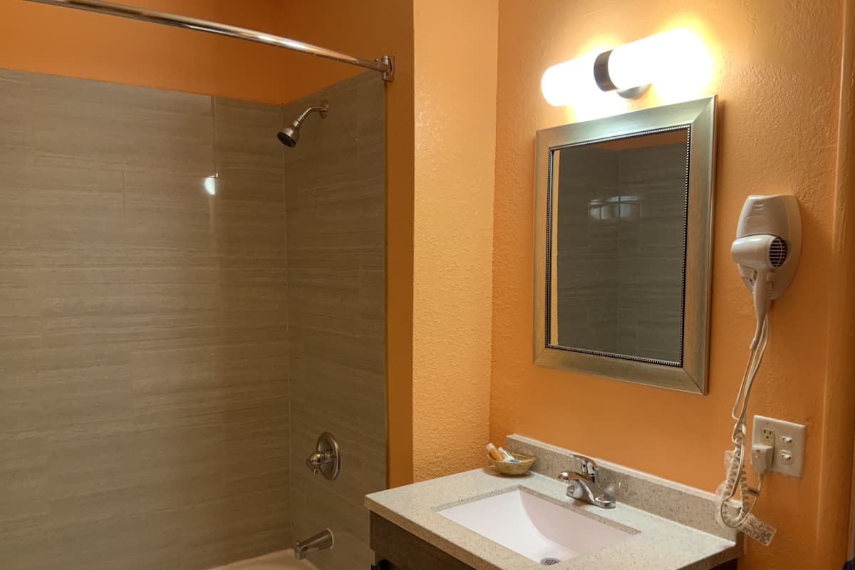 Une salle de bain avec une douche à parois de verre, un lavabo avec un miroir au-dessus et un sèche-cheveux fixé au mur.