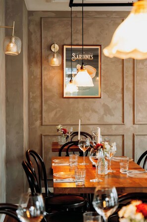 Un comedor con una mesa de madera dispuesta para cuatro personas, un cartel enmarcado en la pared e iluminación colgante.