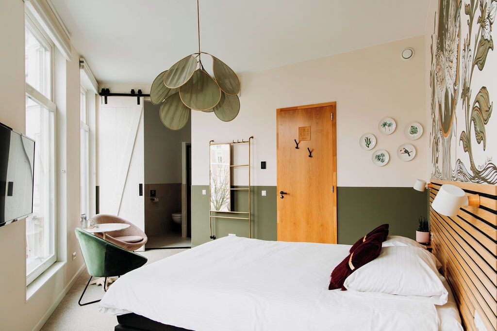 Un dormitorio con cama, lámpara colgante, una silla, una puerta y una pared decorada con placas.