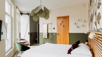 Un dormitorio con cama, lámpara colgante, una silla, una puerta y una pared decorada con placas.