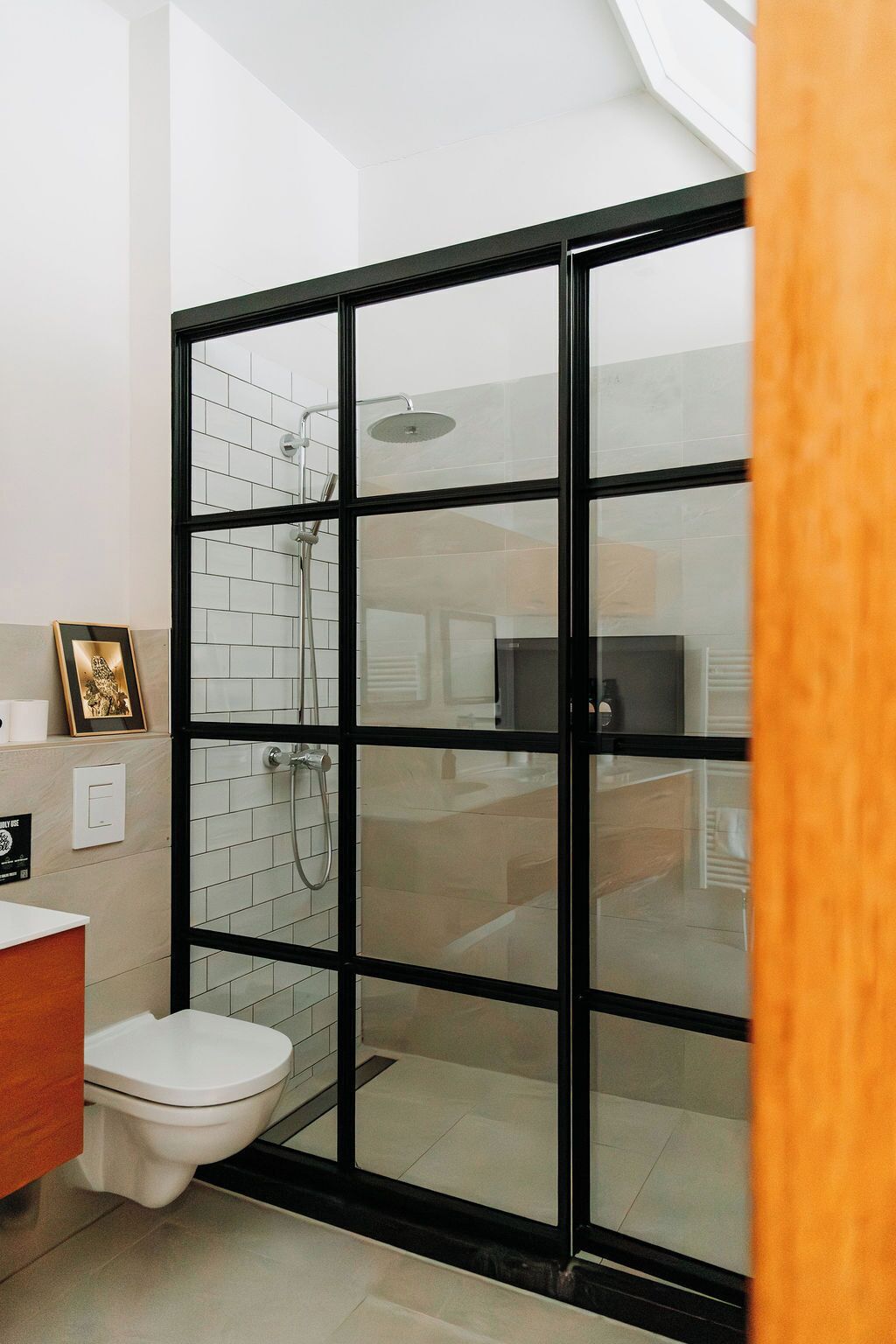 A bathroom with a glass-enclosed shower, a toilet, and a framed picture on the wall.
