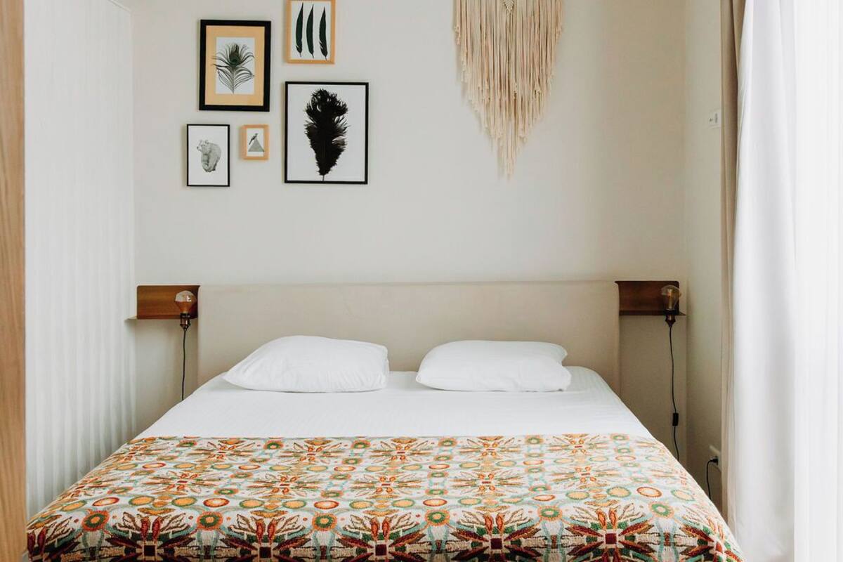 Une pièce avec un lit, des œuvres d’art encadrées accrochées au mur, une décoration murale en macramé et un luminaire au plafond.