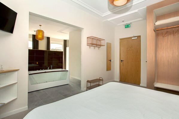 A hotel room with a large bed, a bathtub, a wooden door, and a television on the wall.