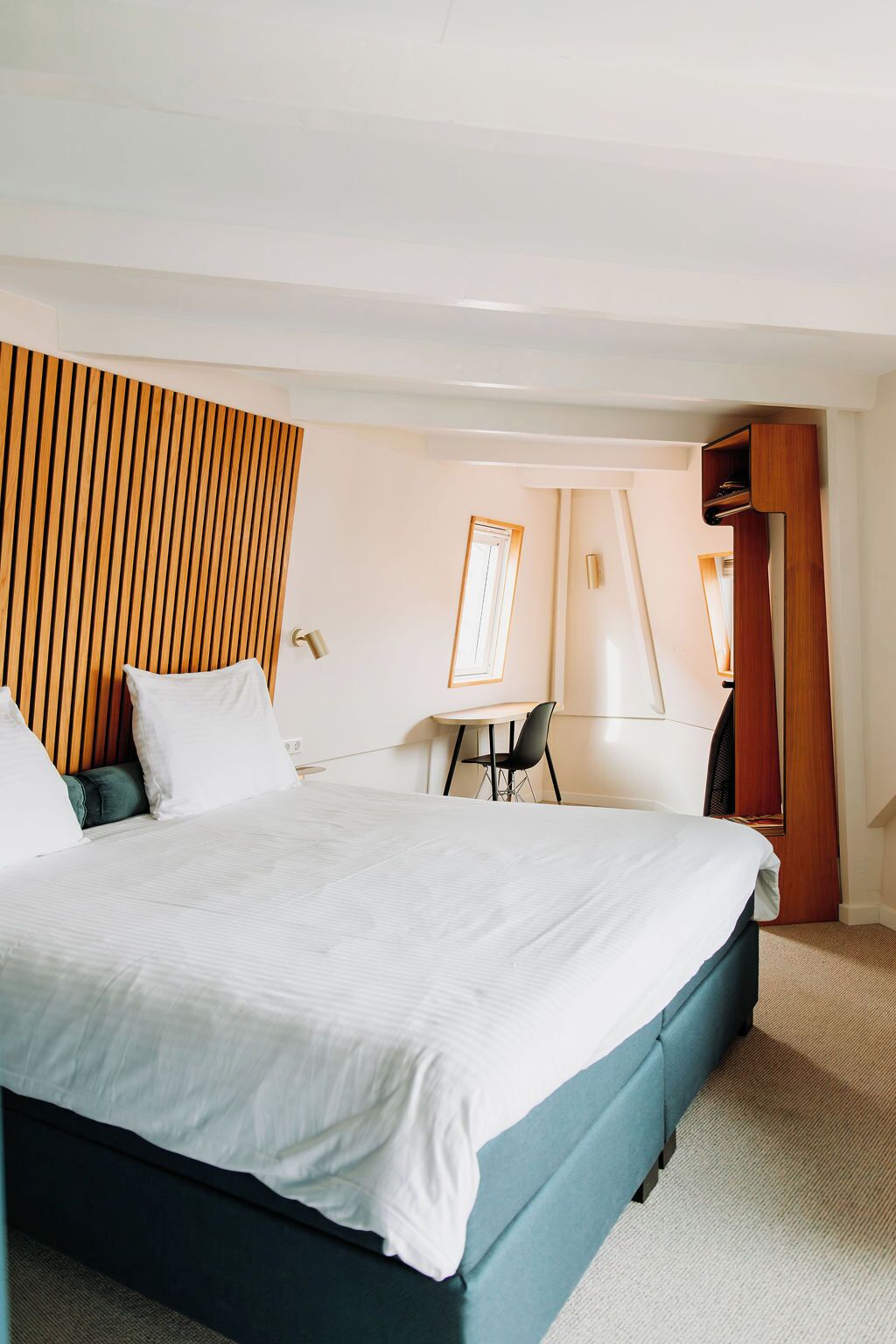 A hotel room with a large bed, a desk, a chair, and a wooden panel wall.