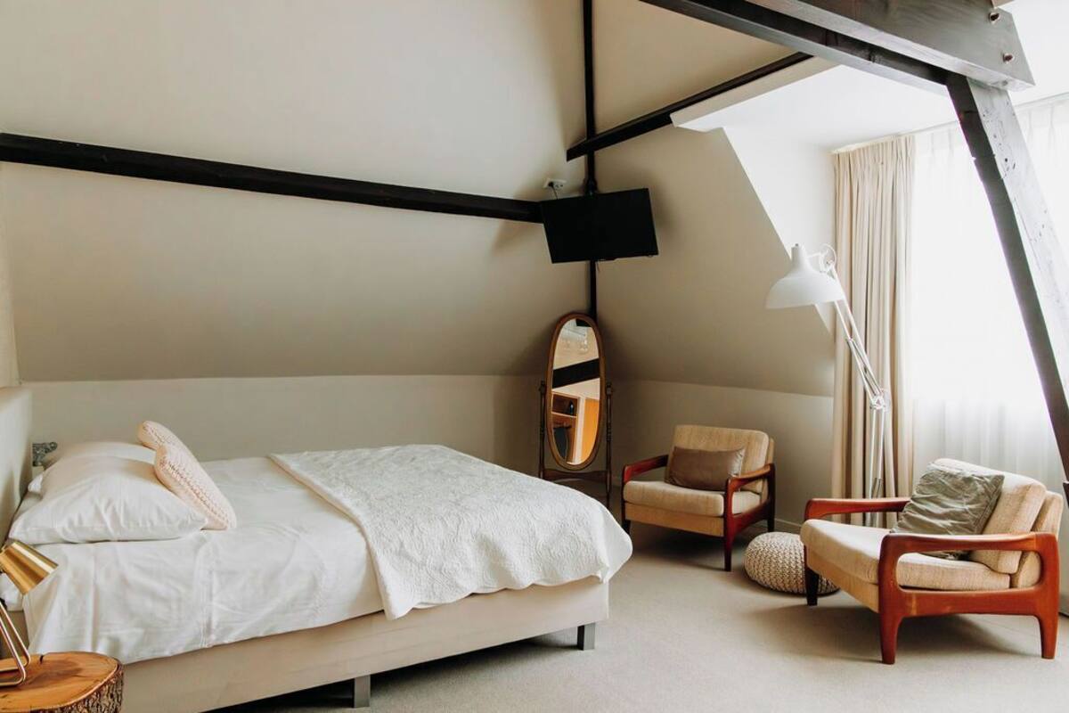 Une chambre à coucher avec un lit, deux chaises, un miroir et un luminaire suspendu.