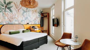 Quarto com uma cama, uma mesinha, duas cadeiras, uma televisão e uma janela.