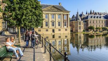 Un bâtiment historique à l’architecture classique, un plan d’eau qui reflète son image à l’avant, et une promenade piétonne agrémentée de bancs.