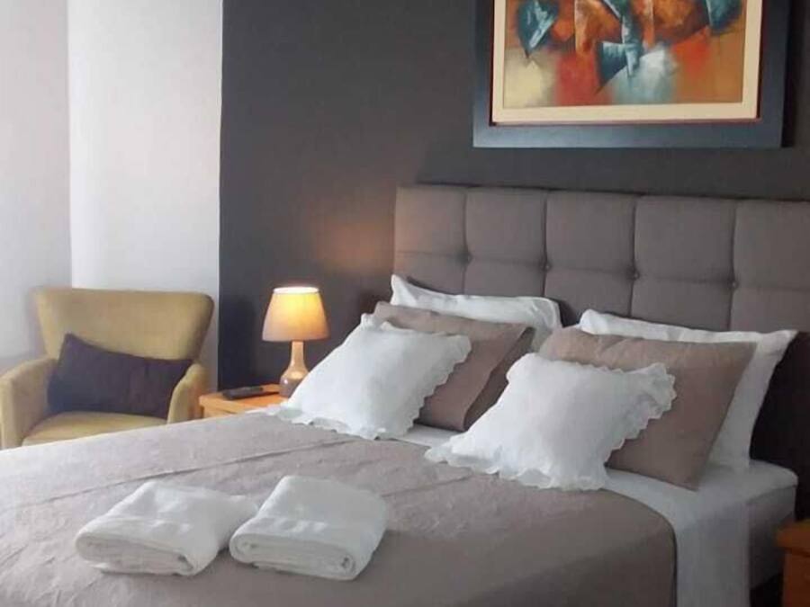 Una cama bien hecha con sábanas y almohadas blancas, cabecera gris y un cuadro abstracto moderno sobre ella.