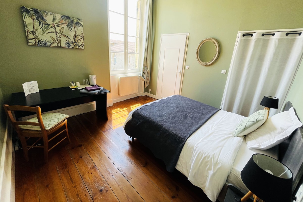Un dormitorio con una cama, un escritorio, una silla, una ventana con cortinas y un espejo colgado en la pared.