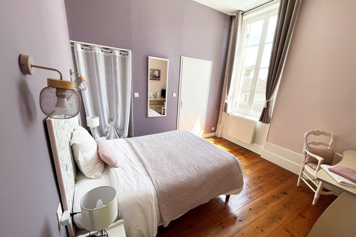 Un dormitorio con cama, mesita de noche, lámpara, espejo y una silla.