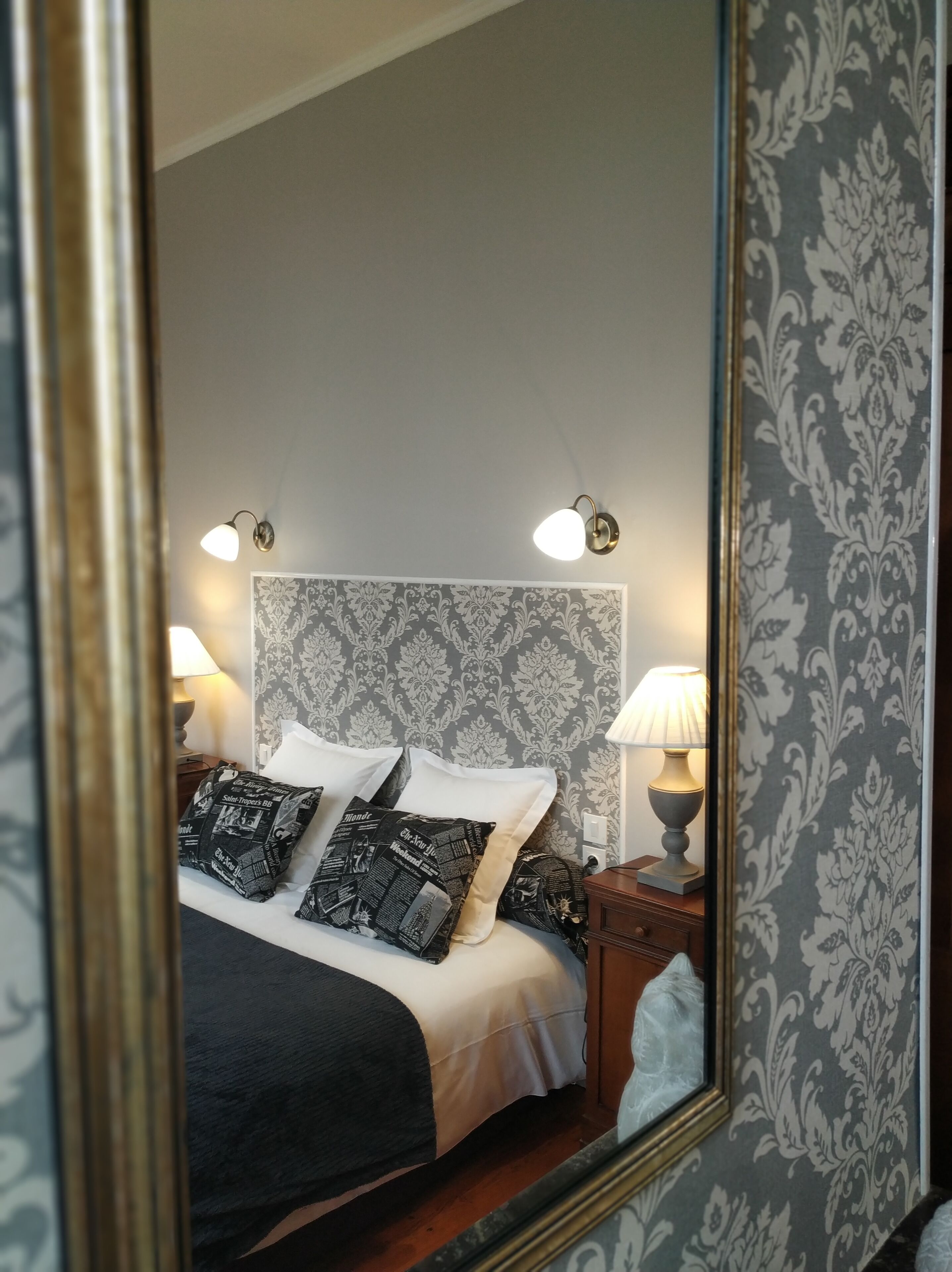 Una cama bien hecha con almohadones estampados, un cabecero con diseño decorativo y lámparas de noche.