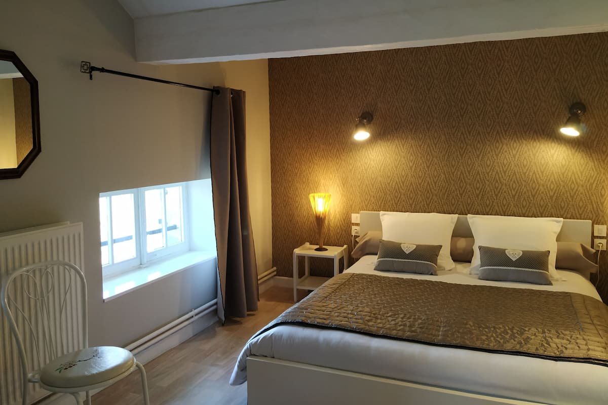 Un dormitorio con una cama, una mesita de noche, una lámpara, una silla y una ventana.
