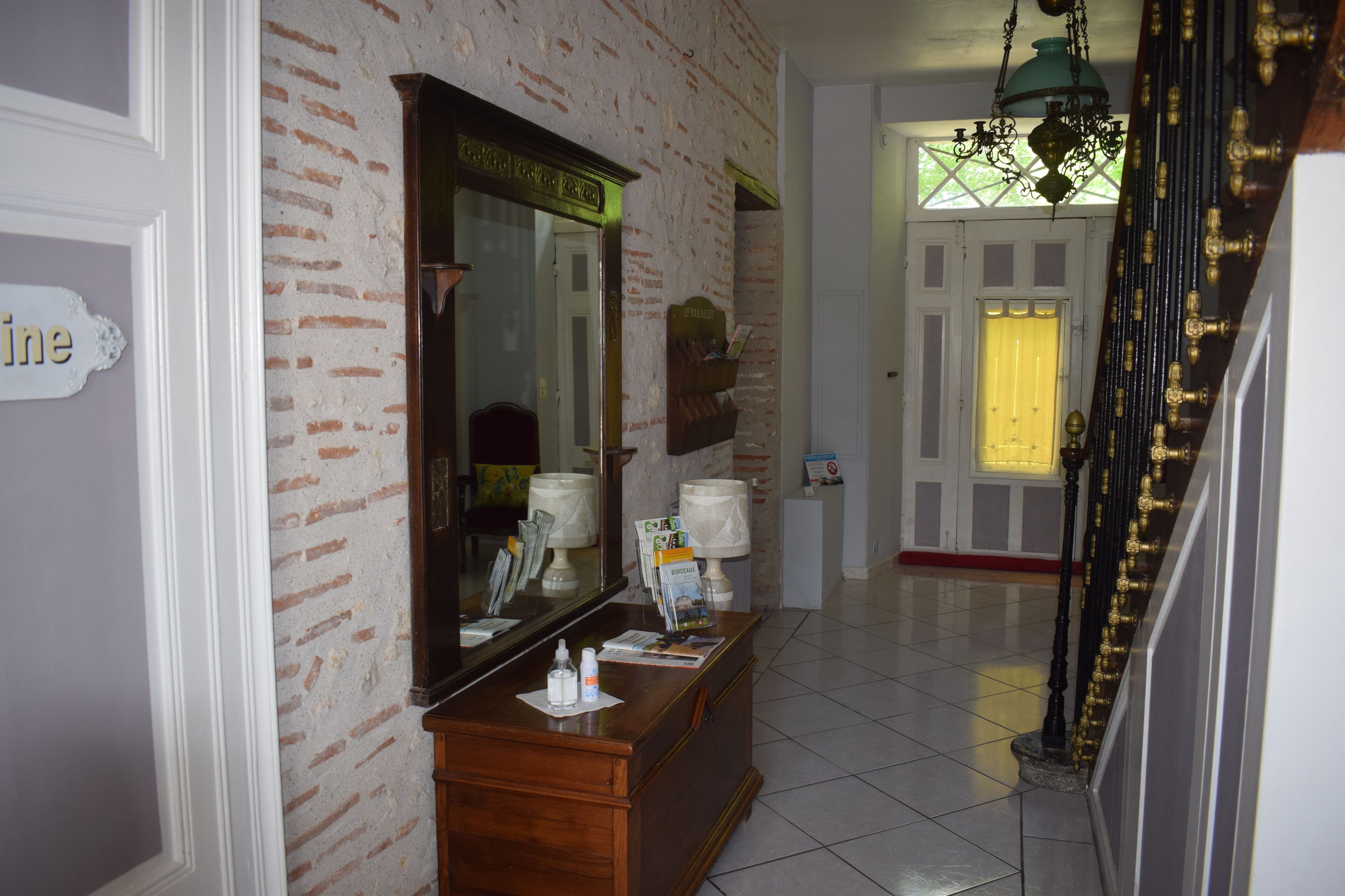 Zona de recepción con pared de ladrillo, mostrador de madera, un espejo grande y una escalera con barandilla.