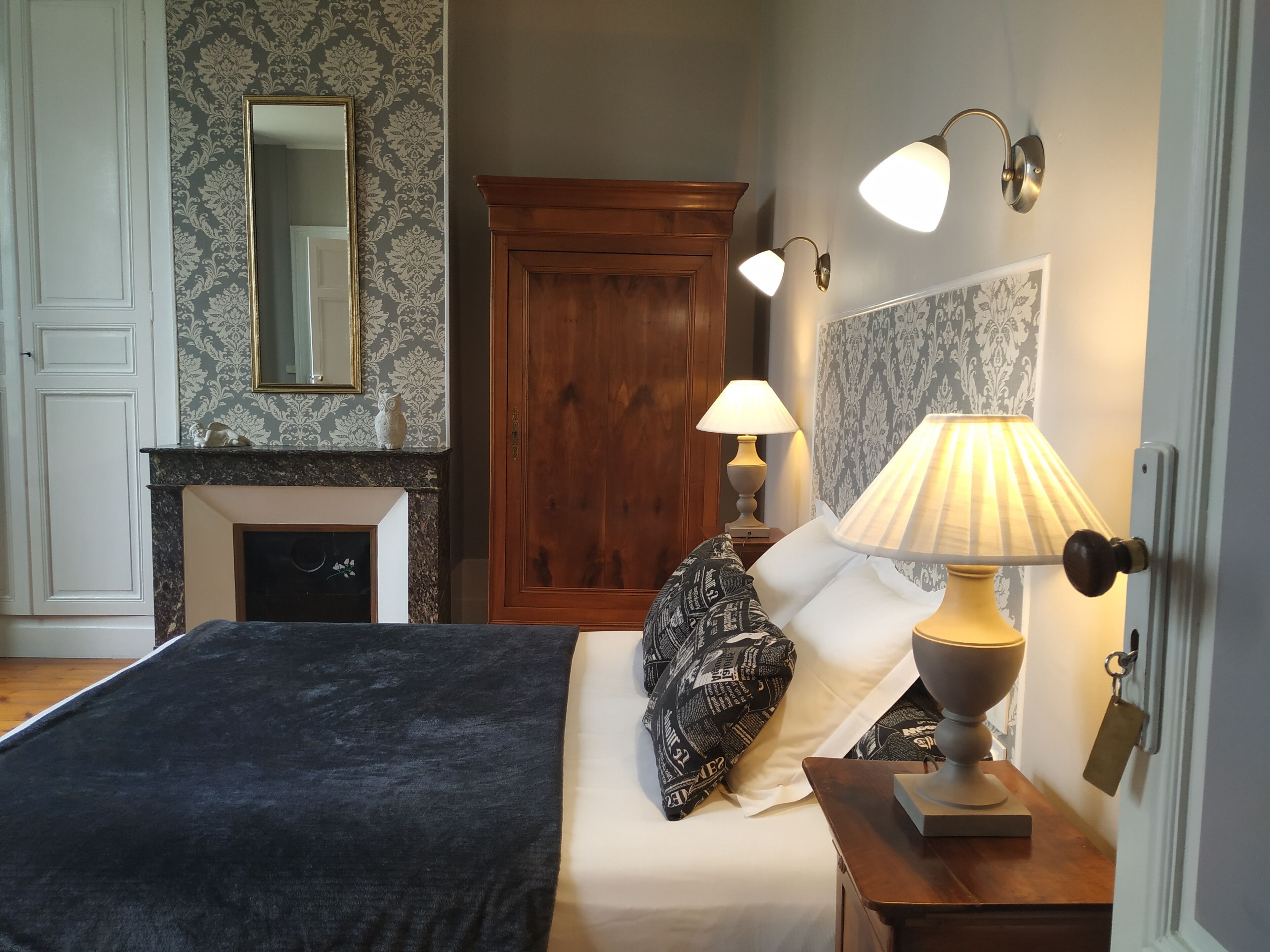 A bedroom with a large bed, a wooden wardrobe, a fireplace, and wall-mounted lamps.