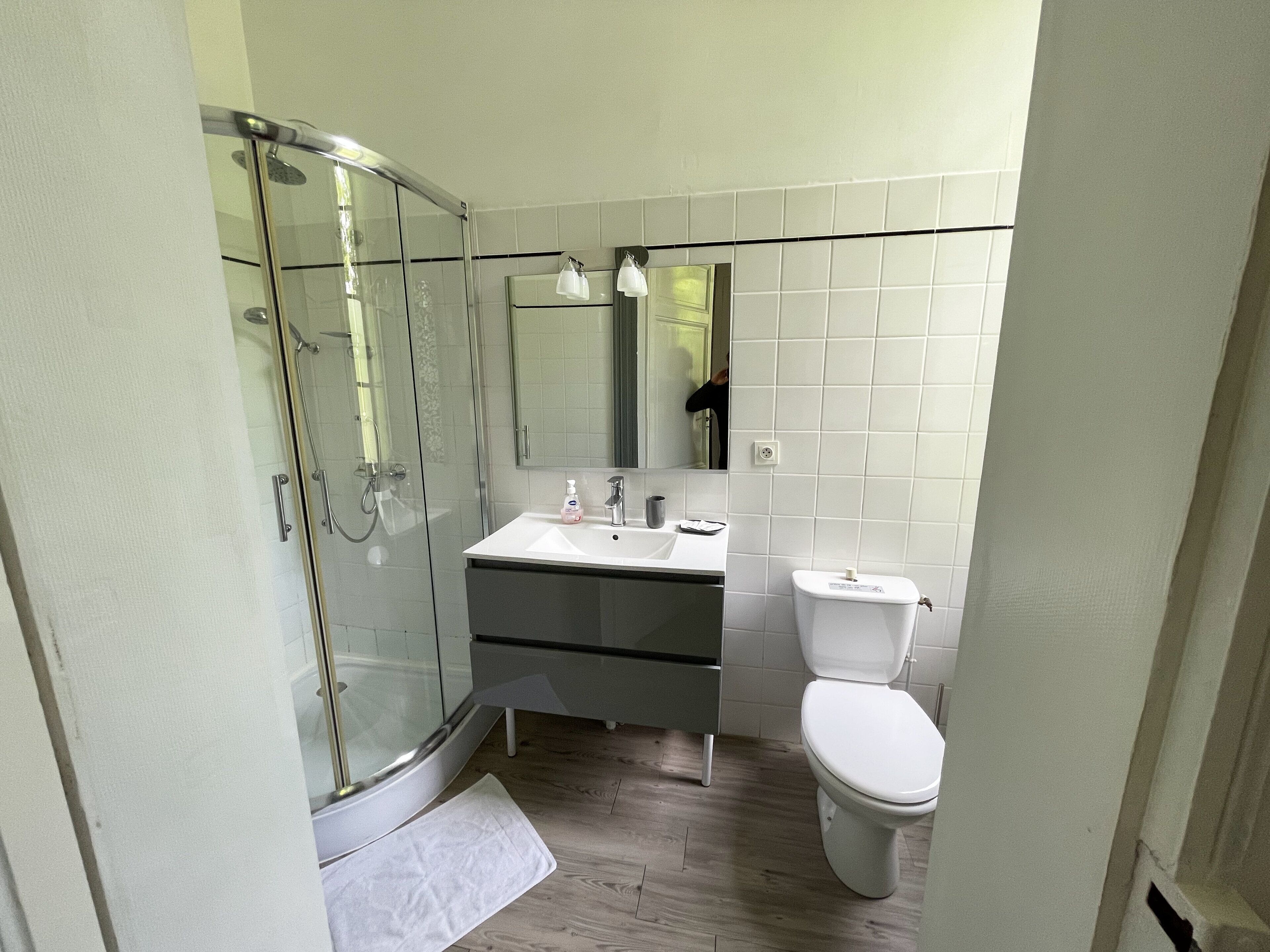 Een badkamer met een douchecabine van glas, een wastafel met spiegel erboven en een toilet.