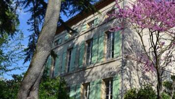 Un edificio a due piani con persiane verdi, circondato da alberi e un albero in fiore.