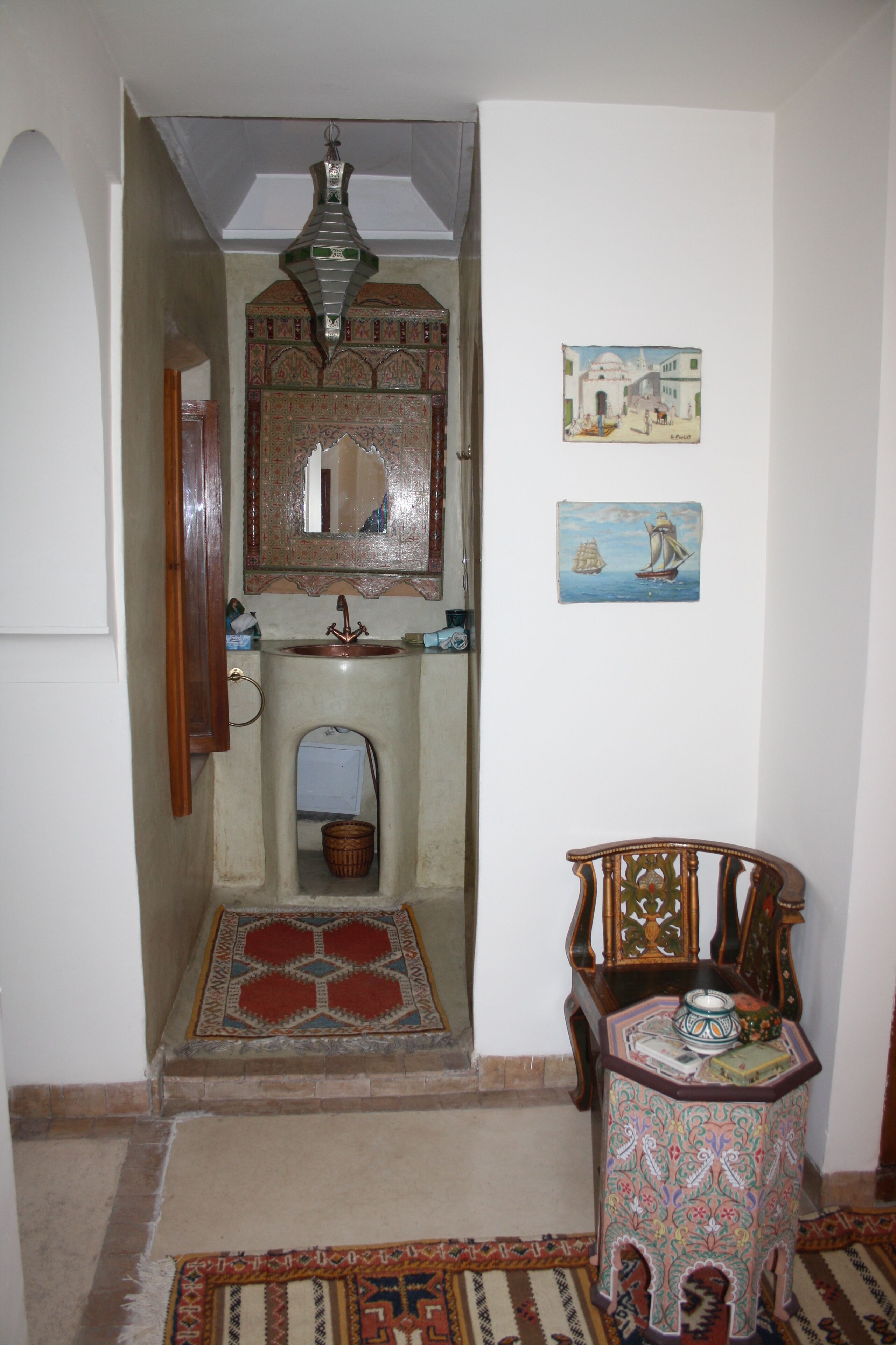 Un interior tradicional con una silla de madera, una mesita, un espejo y un cuadro colgado en la pared.