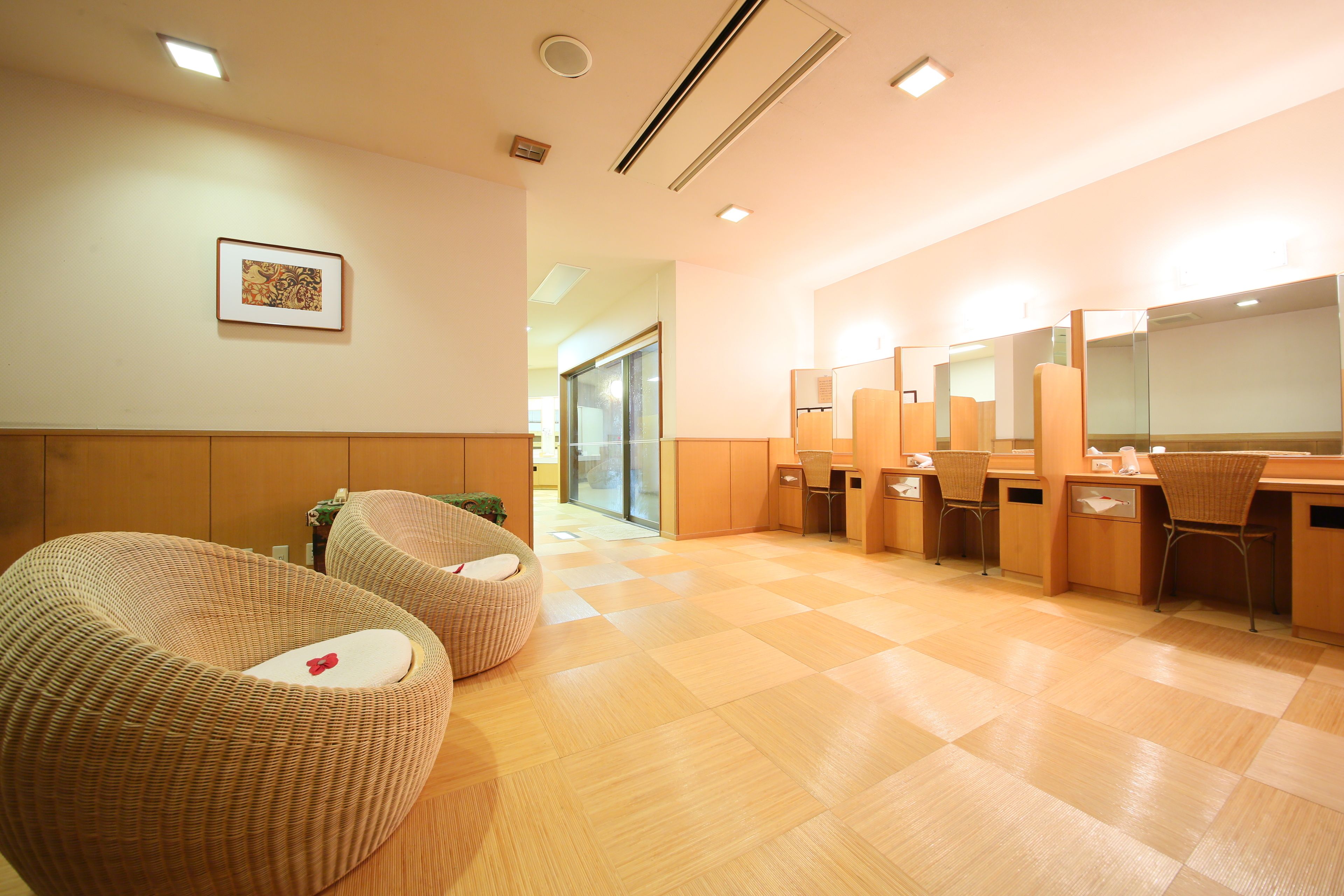 A modern bathroom with wooden flooring, two wicker chairs, a framed picture on the wall, and a mirror above the sink.