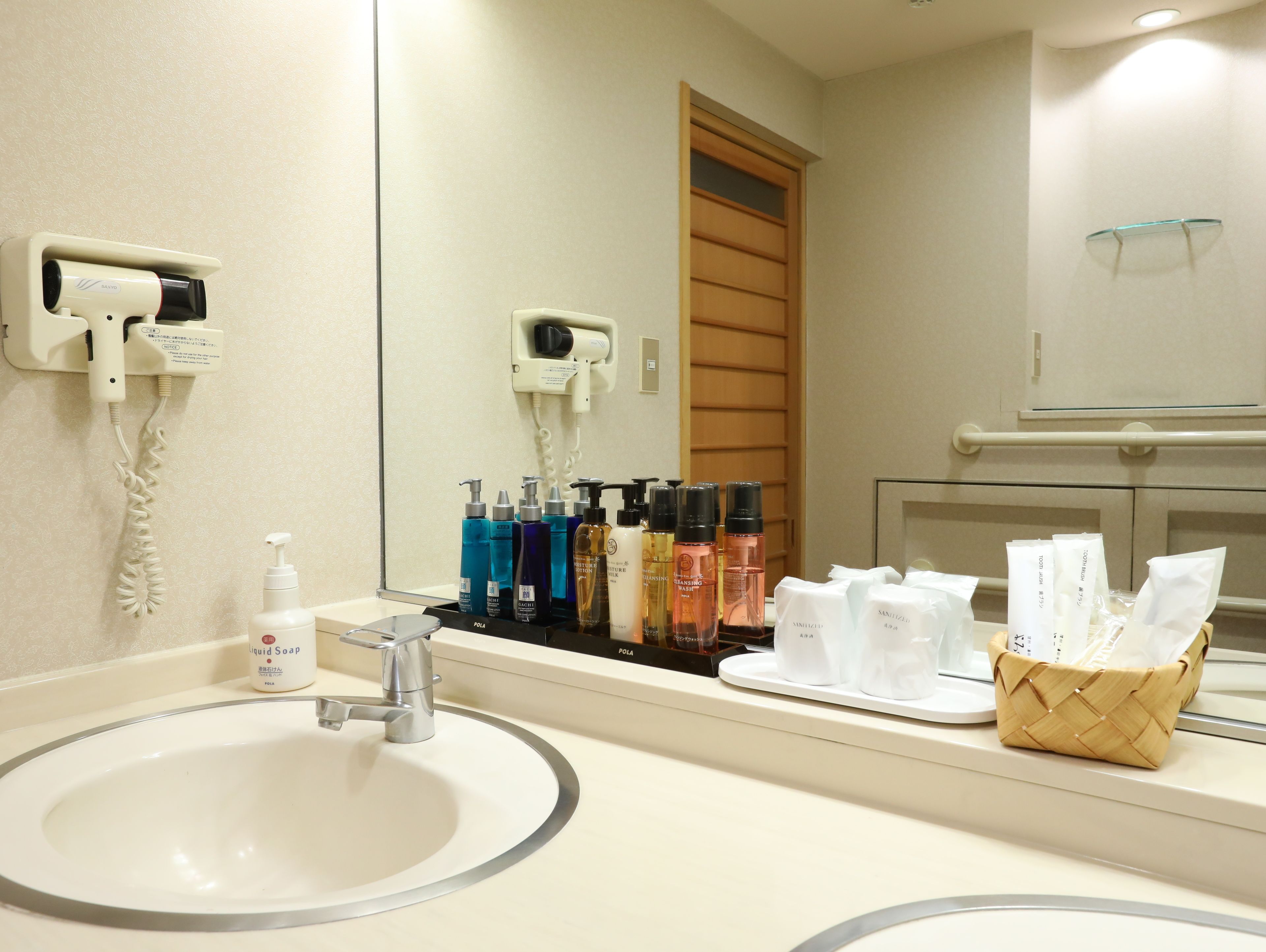 A hotel bathroom with a sink, mirror, hairdryer, and various toiletries.