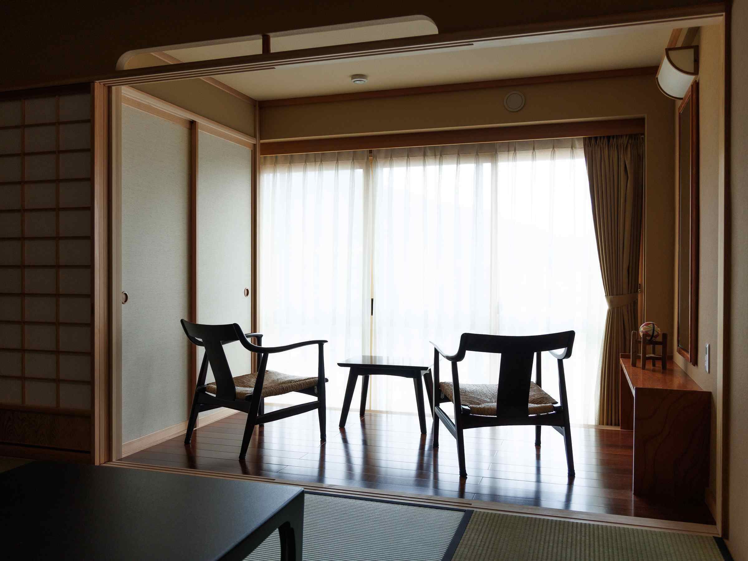 A room with a sliding door, two chairs, a small table, and a view through sheer curtains.